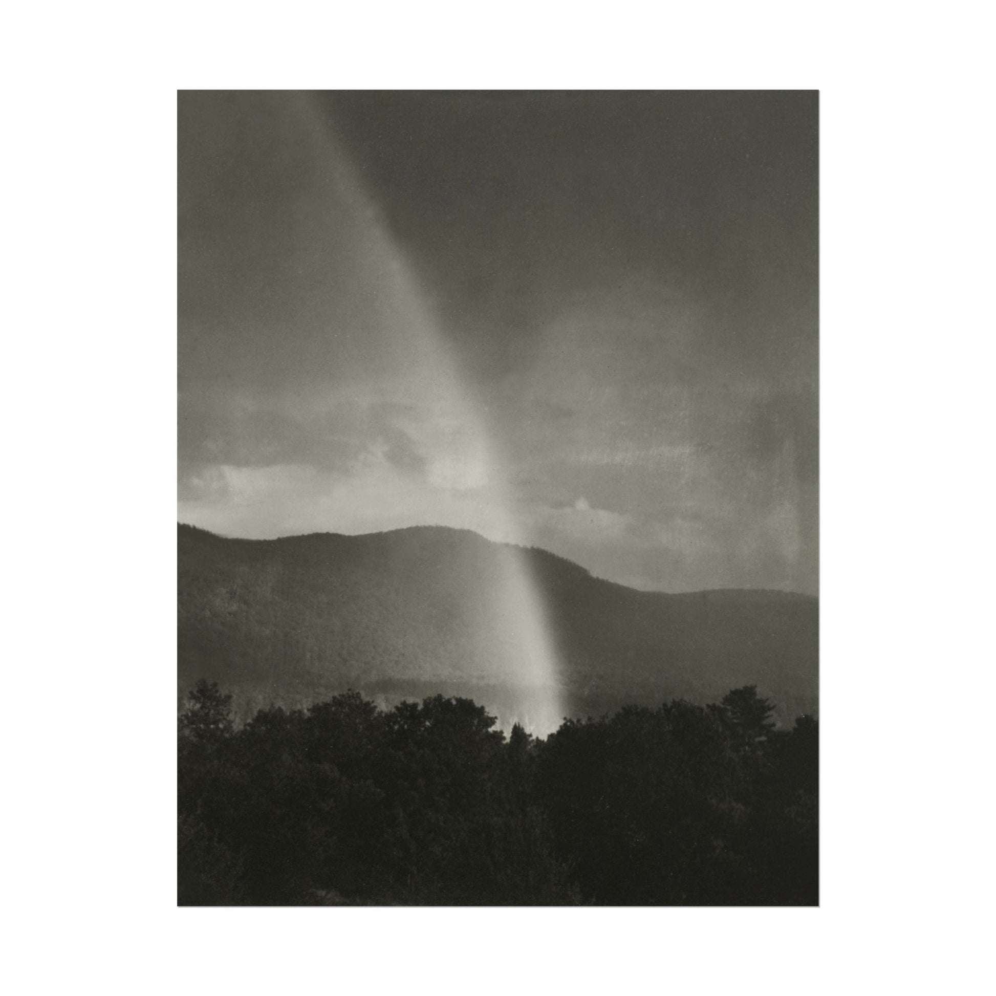 Black-and-white photograph of a rainbow illuminating dark mountains.